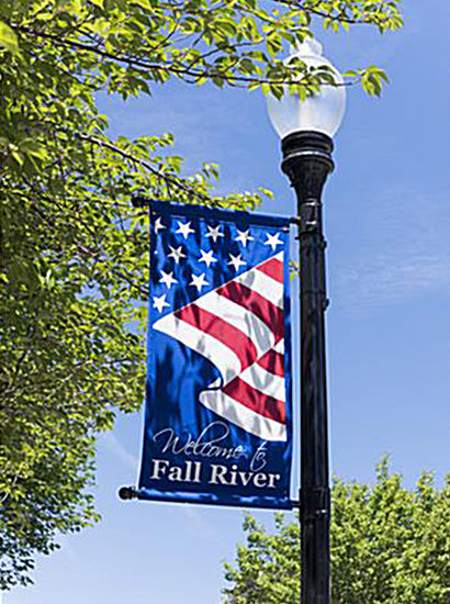 American flag banner on a lamp post with 'Welcome to Fall River' text, against a blue sky.