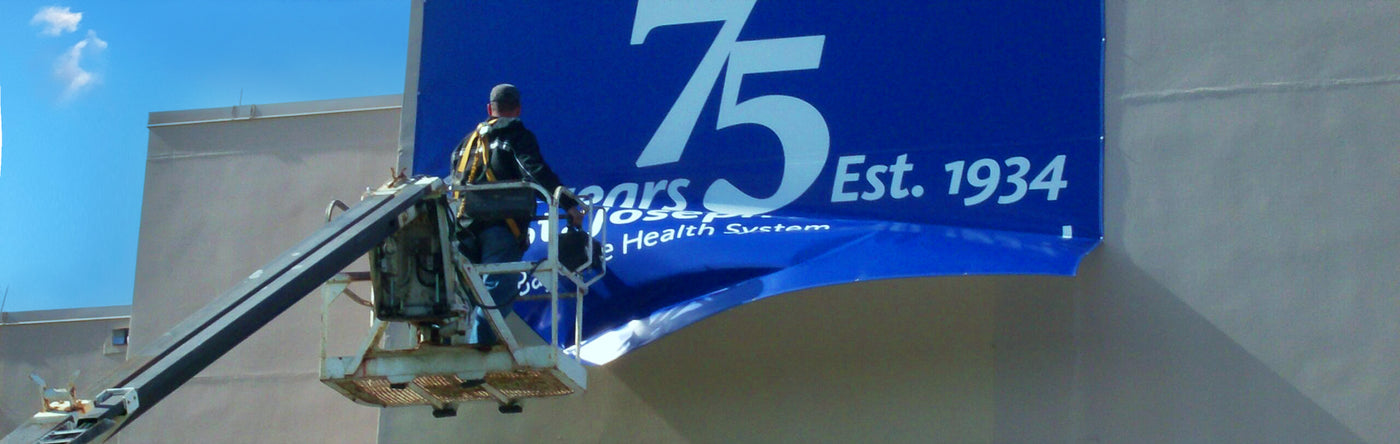 Person installing a large blue banner with '75 Est. 1934' text, mounted on a building.