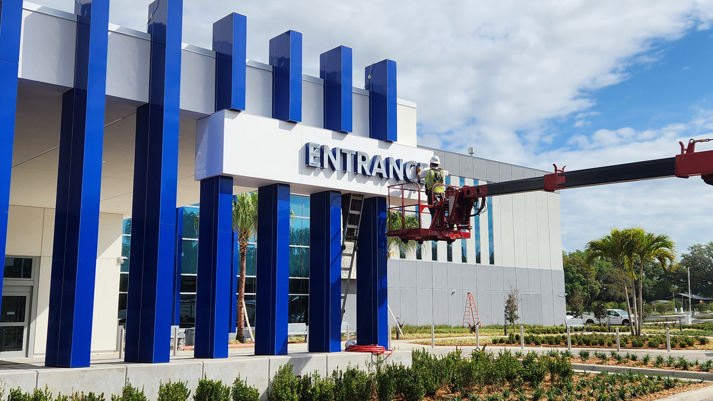Sign-Age employee in cherry picker installing channel letters on an exterior building wall against a blue sky.