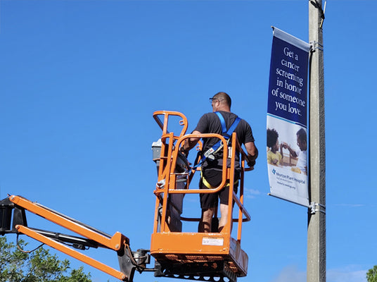 Sign-Age employee on a cherry picker installing a banner with a clear blue sky background