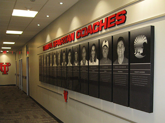 Wall with 'YSU Spartan Coaches' acrylic recognition plaques and portraits of coaches in a hallway.