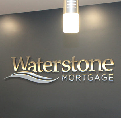 Waterstone Mortgage logo metal dimensional sign on a dark wall with a light fixture above.