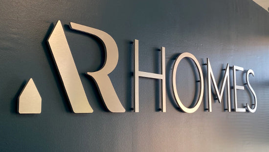 AR Homes dimensional metal letters and logo with standoffs on a dark wall