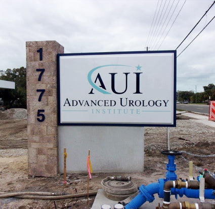 Sign for AUI Advanced Urology Institute with address on illuminated pan face sign mounted on monument, at a construction site.