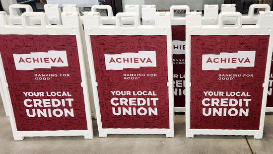 Three Achieva A-frame signs for a local credit union on a sidewalk.