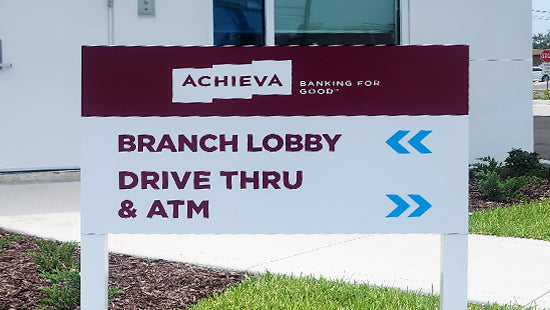 Directional post and panel sign pointing to Achieva Credit Union branch lobby, drive thru, and ATM.