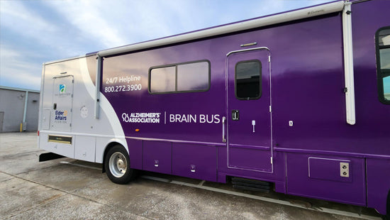 Purple and white vehicle wrap on Alzheimer's Association Brain Bus on a concrete surface with a building in the background.