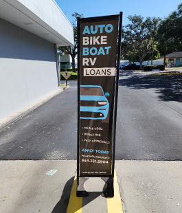 Outdoor banner for auto, bike, boat, RV loans on a sidewalk.