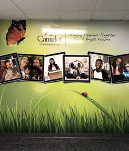 Wall mural with framed photos of people and a butterfly on a green grass-like background.