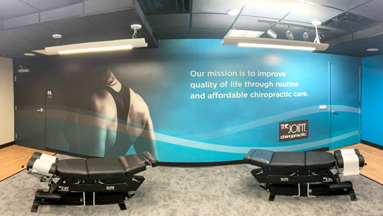 Chiropractic office interior with two treatment tables and a wall mural.