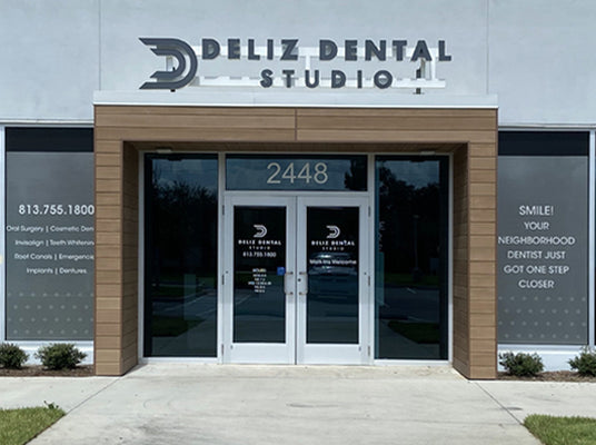 Front entrance of Deliz Dental Studio with glass doors and window graphics signage.