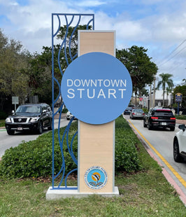 Downtown Stuart monument sign with blue and beige colors on a street background