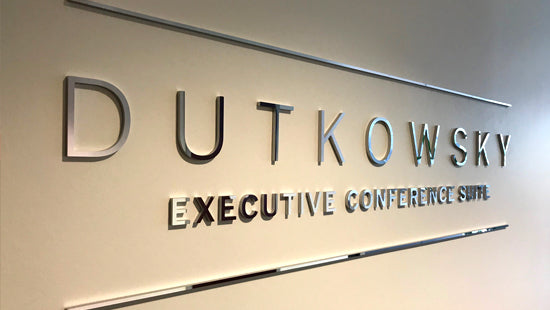 Metallic 'DUTKOWSKY EXECUTIVE CONFERENCE SUITE' metal interior sign on a beige wall.