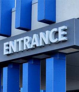 Illuminated channel leter sign with 'ENTRANCE' text on a building facade with blue columns