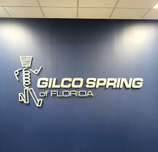 Dimensional logo of Gilco Spring of Florida on a blue wall.