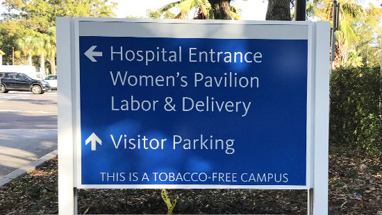 Hospital directional sign with text indicating entrance, women's pavilion, labor & delivery, visitor parking, and tobacco-free campus.