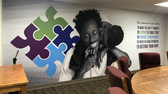 Wall mural of a person with a microphone in front of colorful puzzle pieces and text on a wall.
