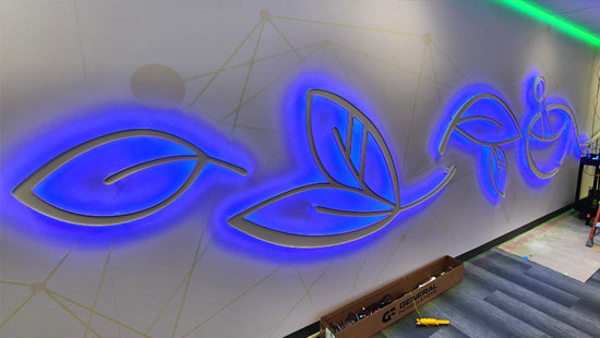 Installation of illuminated dimensional graphics sign on a large wall with tools visible on floor below.