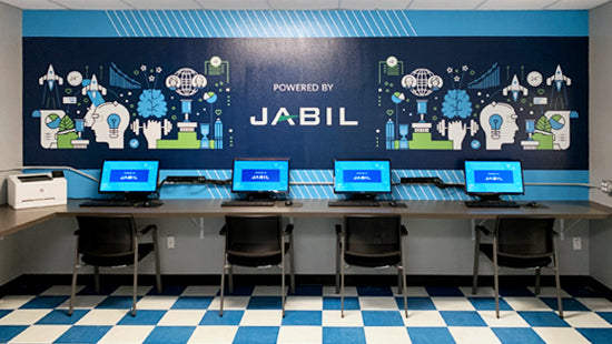 Workstation setup with multiple computers in front of a Jabil-branded wall mural.