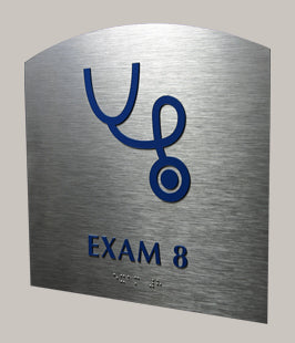 Metal ADA sign with blue stethoscope symbol and 'EXAM 8' text in tactile letters and braille on a silver background
