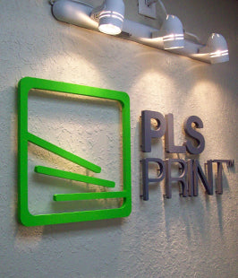 PLS Print dimensional letters and logo sign with green and black design elements mounted on a wall with standoffs.
