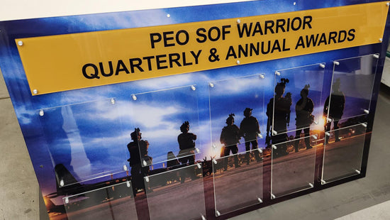Award display with 'PEO SOF Warrior Quarterly & Annual Awards' text and silhouettes of people against a blue sky.