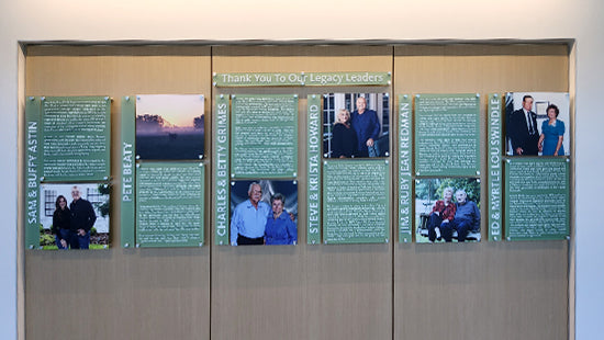 Donor Plaque system of framed photographs and text of people, against a wooden backdrop