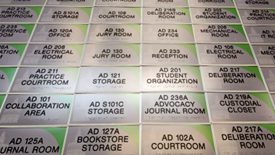 Collection of ADA room name signs on a grid, each labeled with different room names in tactile text and Braille.
