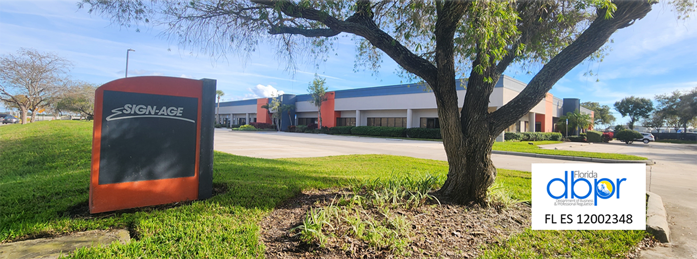 Commercial building with a 'Sign-Age' monument sign in front, surrounded by trees and grass.