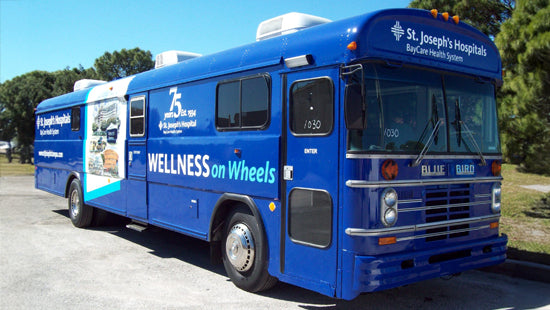 Bus with 'Wellness on Wheels' and 'St. Joseph's Hospitals' full vehicle wrap branding on a road.