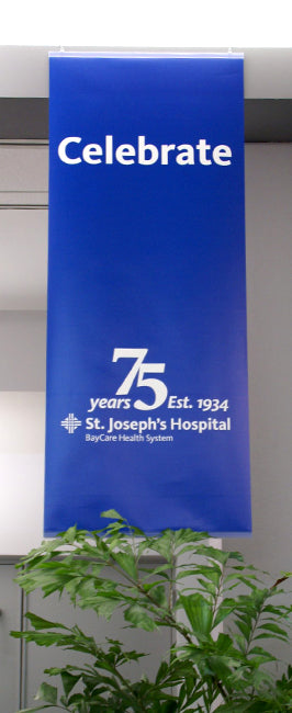 Blue pole banner celebrating St. Joseph's Hospital's 75th anniversary with a plant in the foreground.