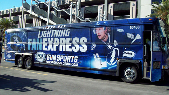 Blue bus with sports team branding on a full vehicle wrap, parked on a city street.
