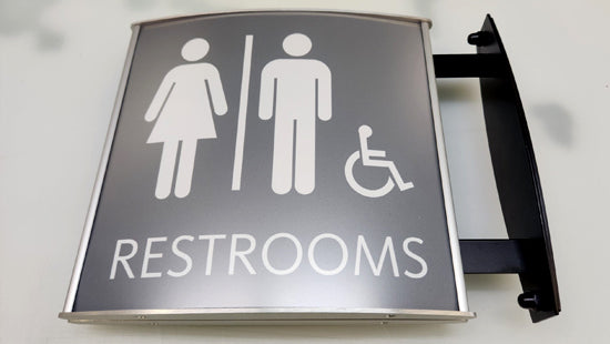 ADA wall sign with gender neutral and disabled access icons on a gray background, reading "Restrooms" in tactile text and Braille