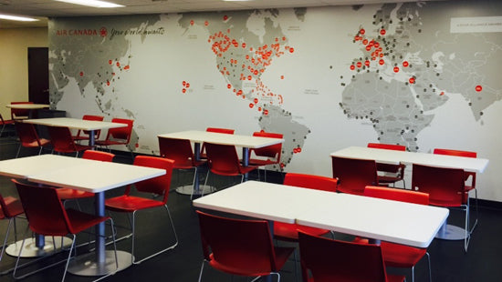 Modern office space with red chairs and white tables in front of a wall mural of a world map with location pins.