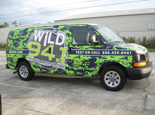 Van with Wild 94.1 branding in a camouflage pattern on a concrete surface.