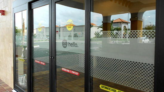 Glass door with 'hello' branding on window film and automatic door warning signs.