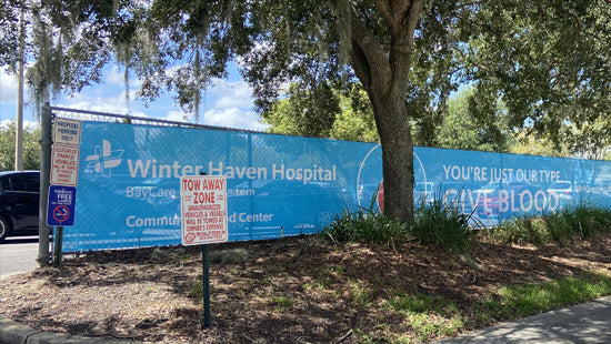 Large fence banners with Winter Haven Hospital branding and various signs in a park-like setting.